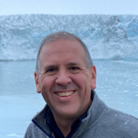 Jared Webb smiling in front of a glacier, wearing a gray fleece in a cold landscape.